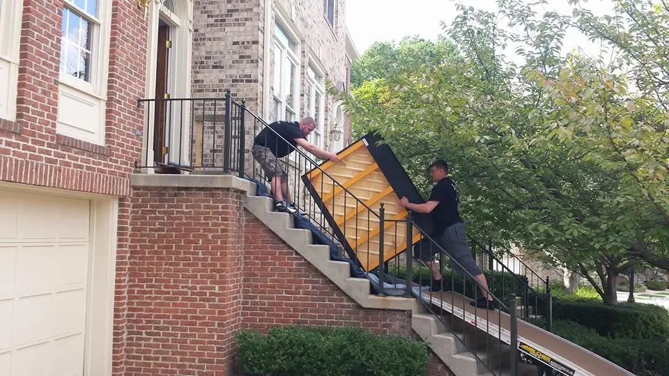 Movers carrying an upright piano up outdoor brick steps