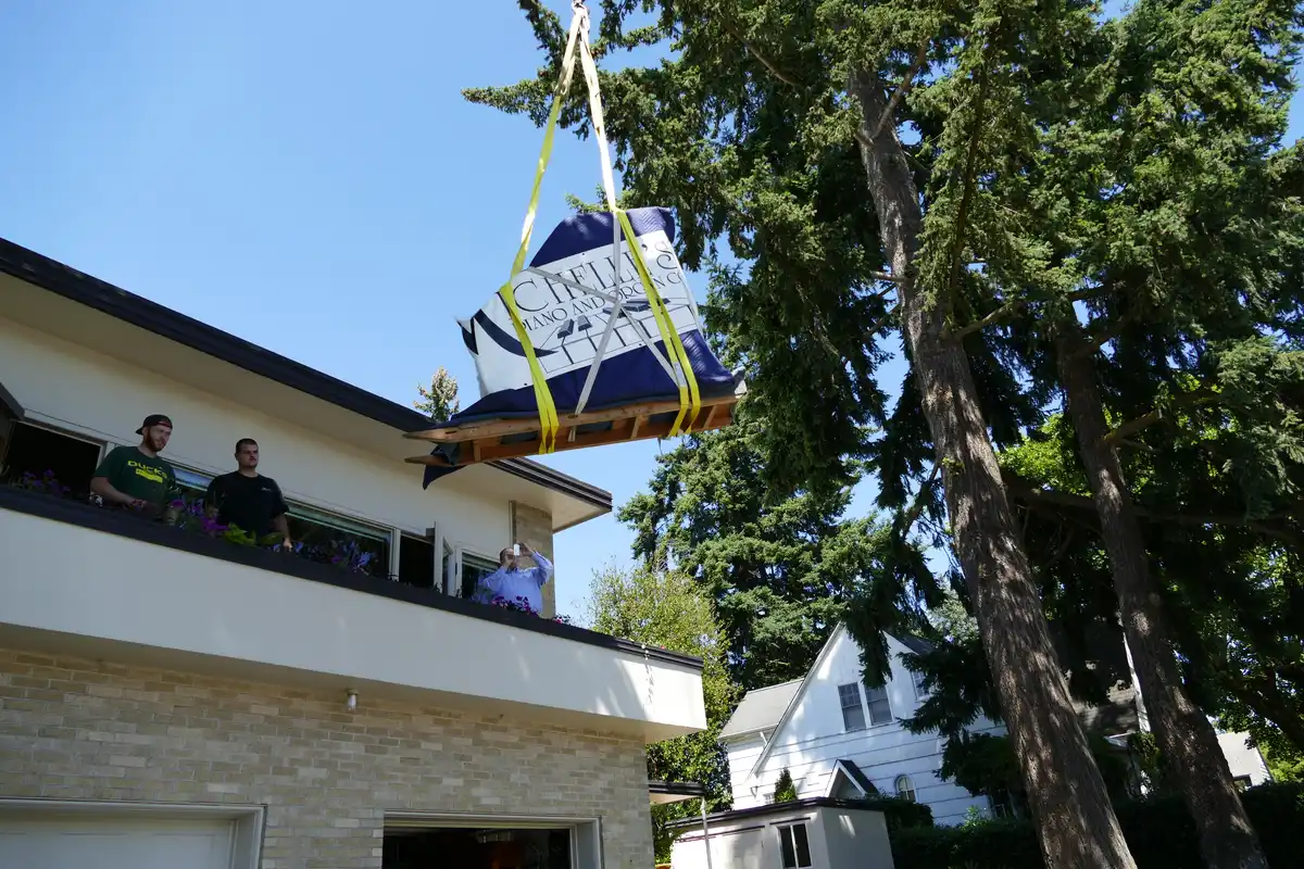 Wrapped piano being lifted by crane beside a house