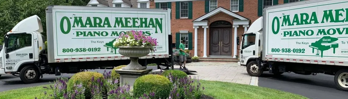 Two piano moving trucks parked outside a house
