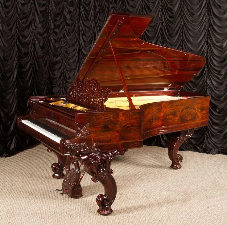 Antique carved rosewood grand piano against a dark curtain
