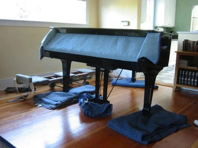 Grand piano being padded with moving blankets before a move